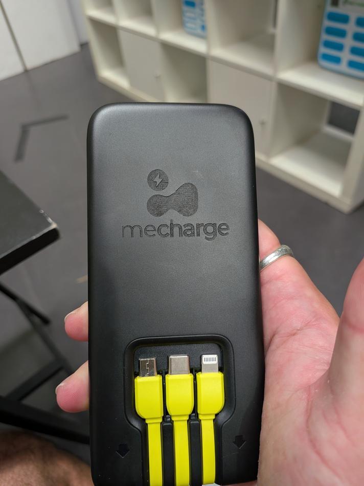 A mecharge powerbank held in one hand, showing the three charging cables built into the base.