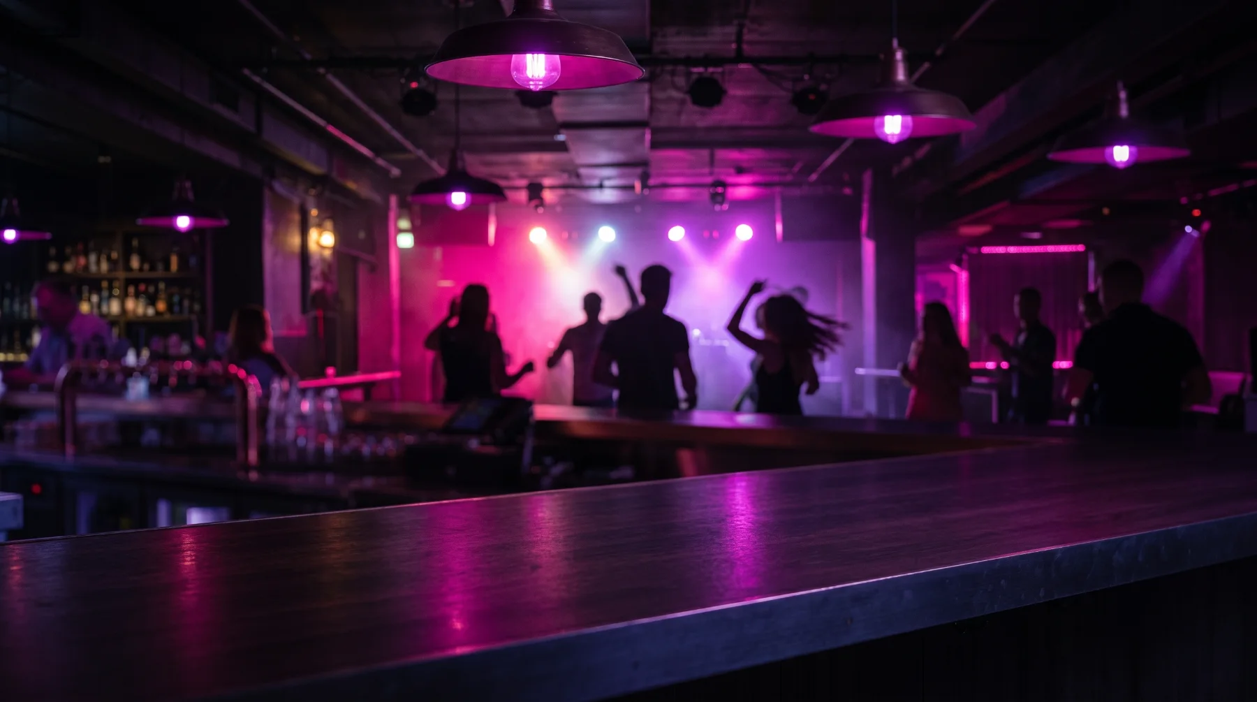 A bar top with a dance floor and magenta stage lighting behind.