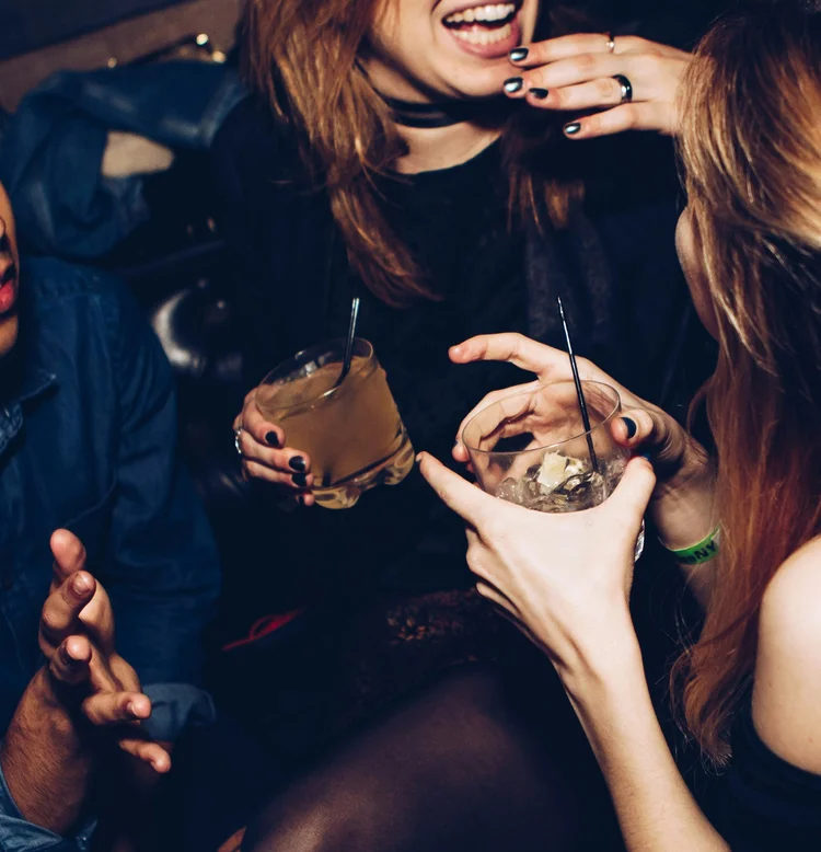 People socializing at a bar, holding drinks, and engaging in conversation.
