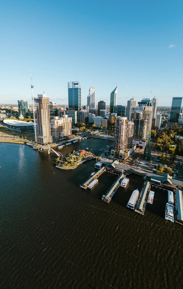 Aerial view of a modern city skyline with tall skyscrapers, a waterfront, and a marina with boats and docks.